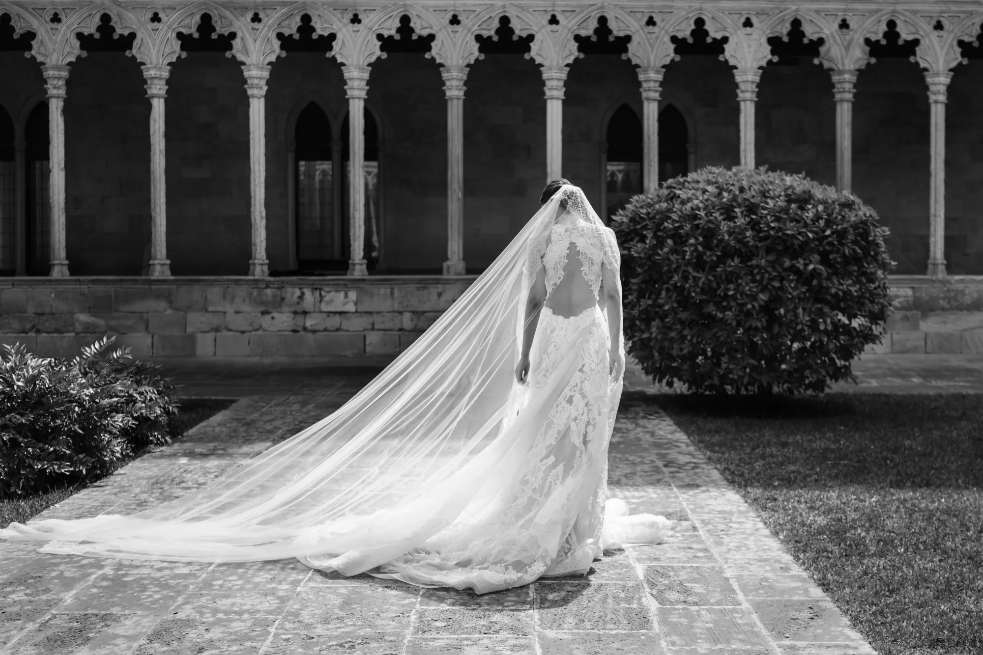 Black and white photo of a bride's long veil trailing before cloister arches