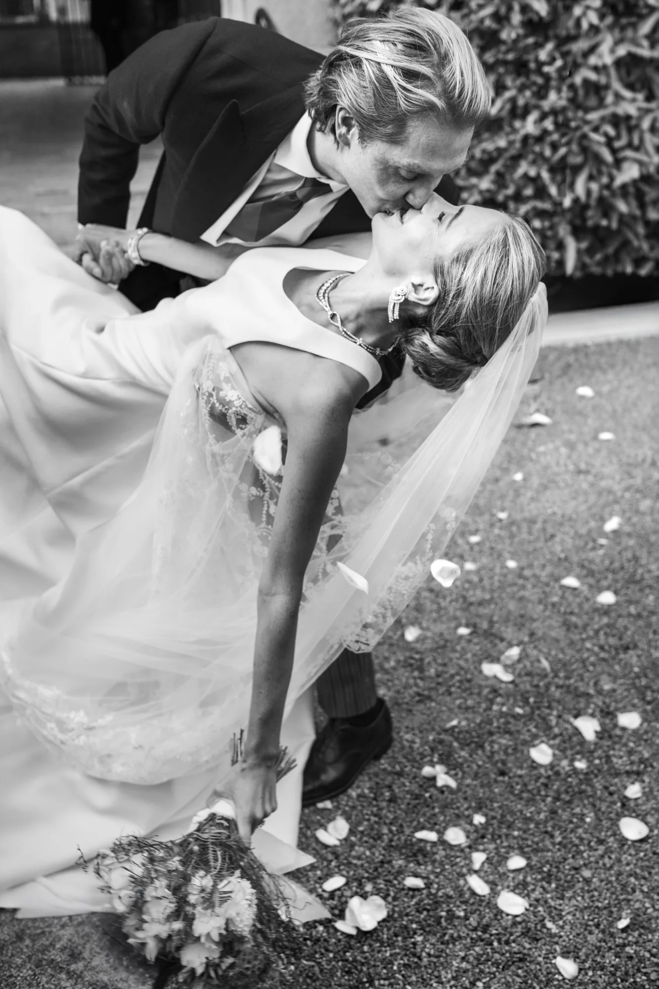 Black and white photo of the groom dipping the bride for a kiss over scattered petals