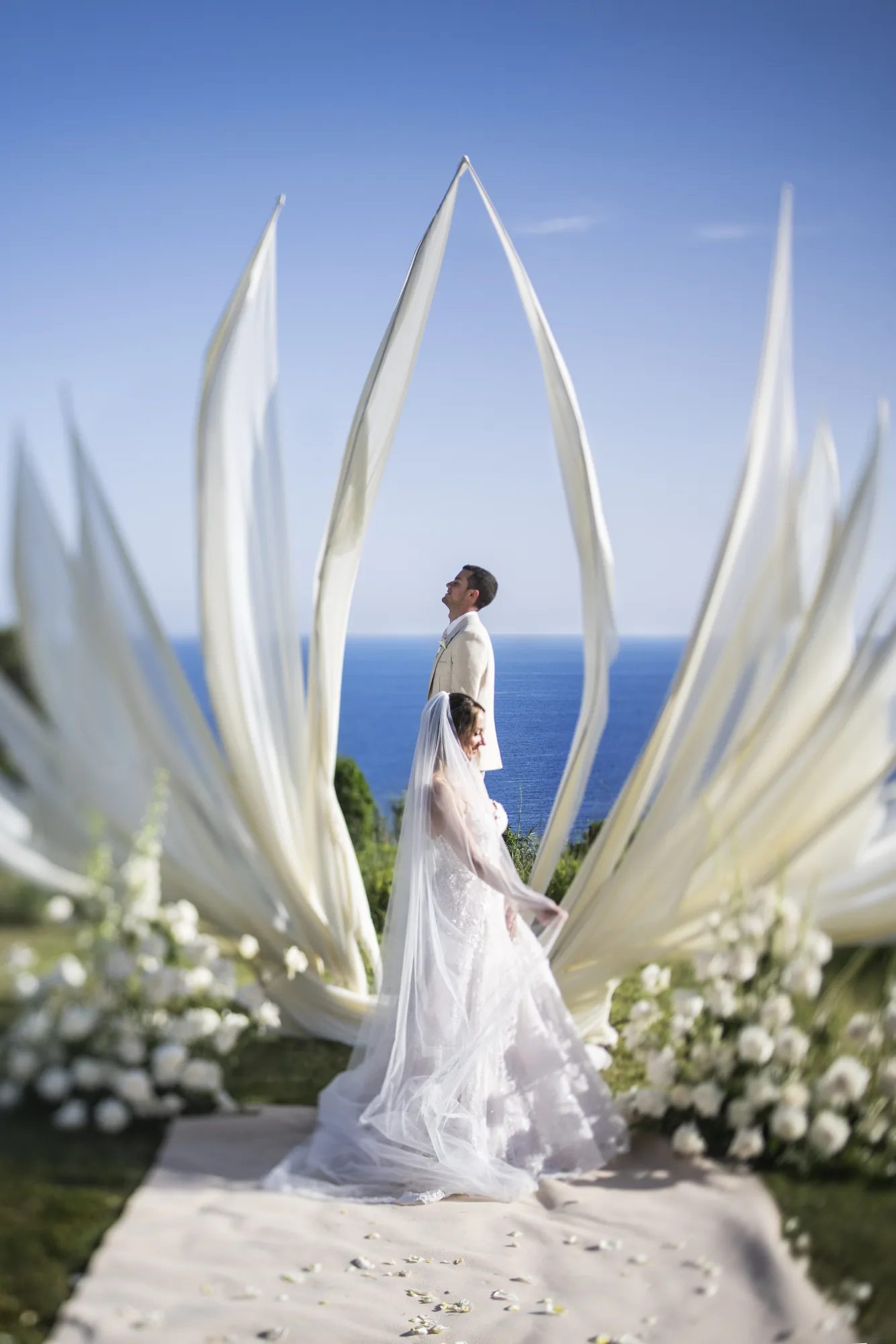 Bride before a white winged sculpture above the sea