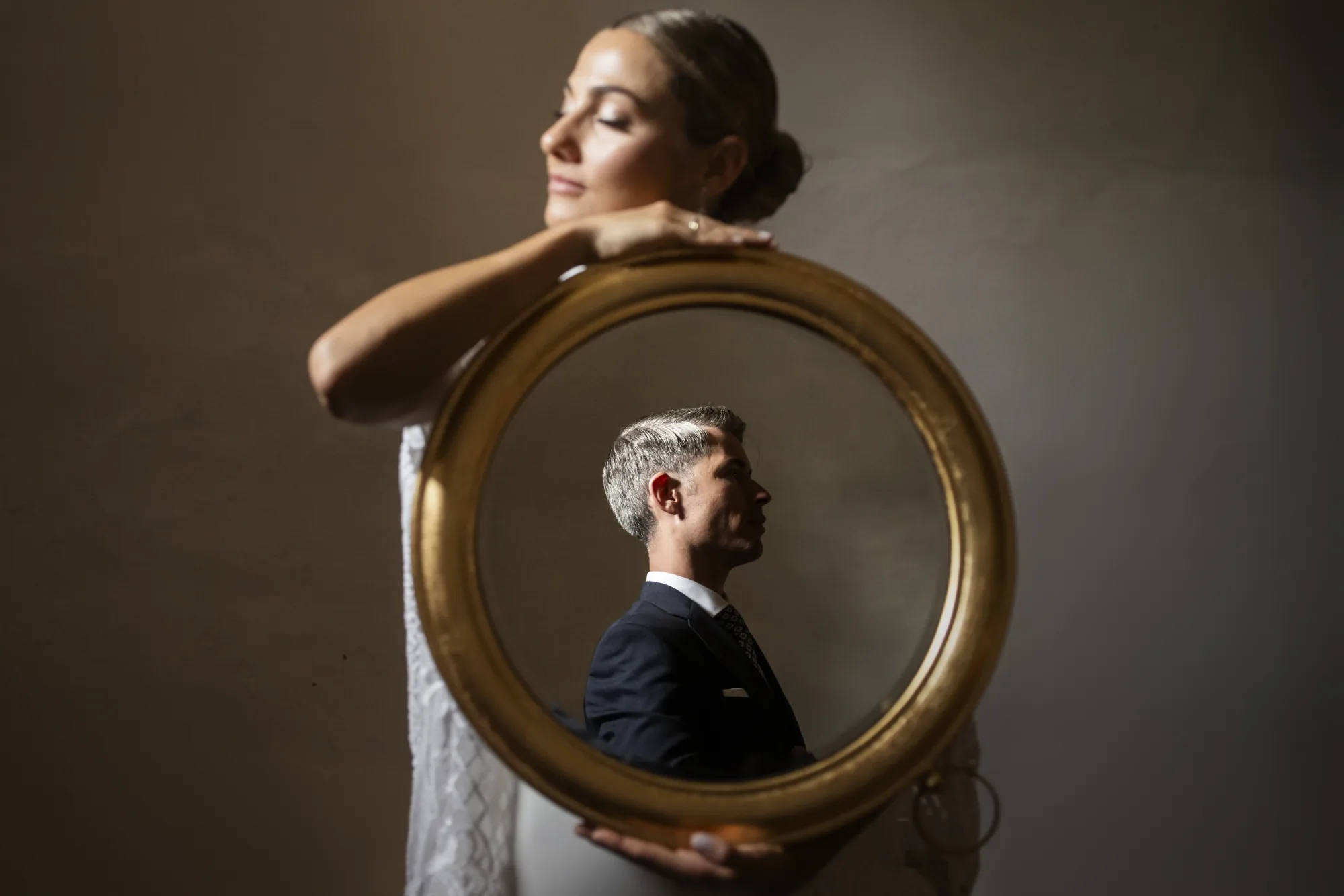 Bride holding a round gilded mirror that reflects the groom