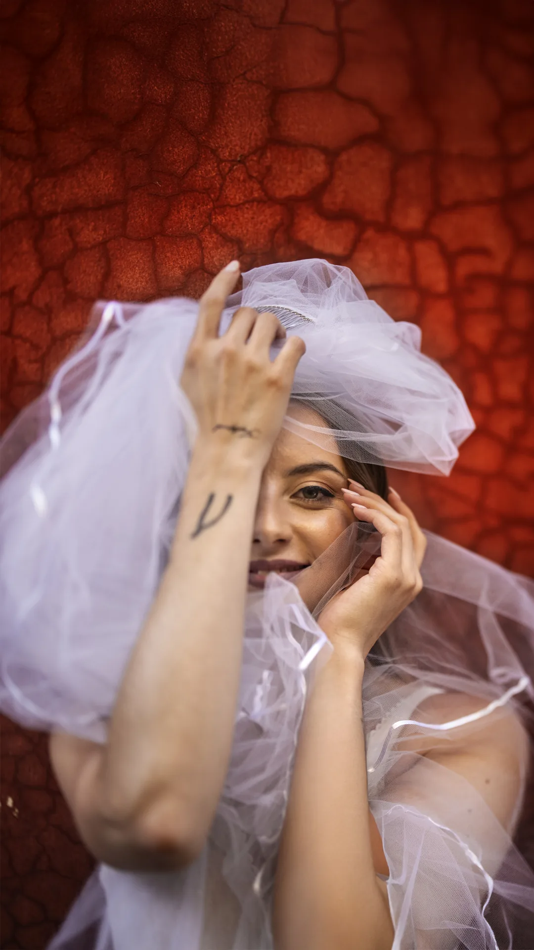 Bride laughing under her veil against a red wall