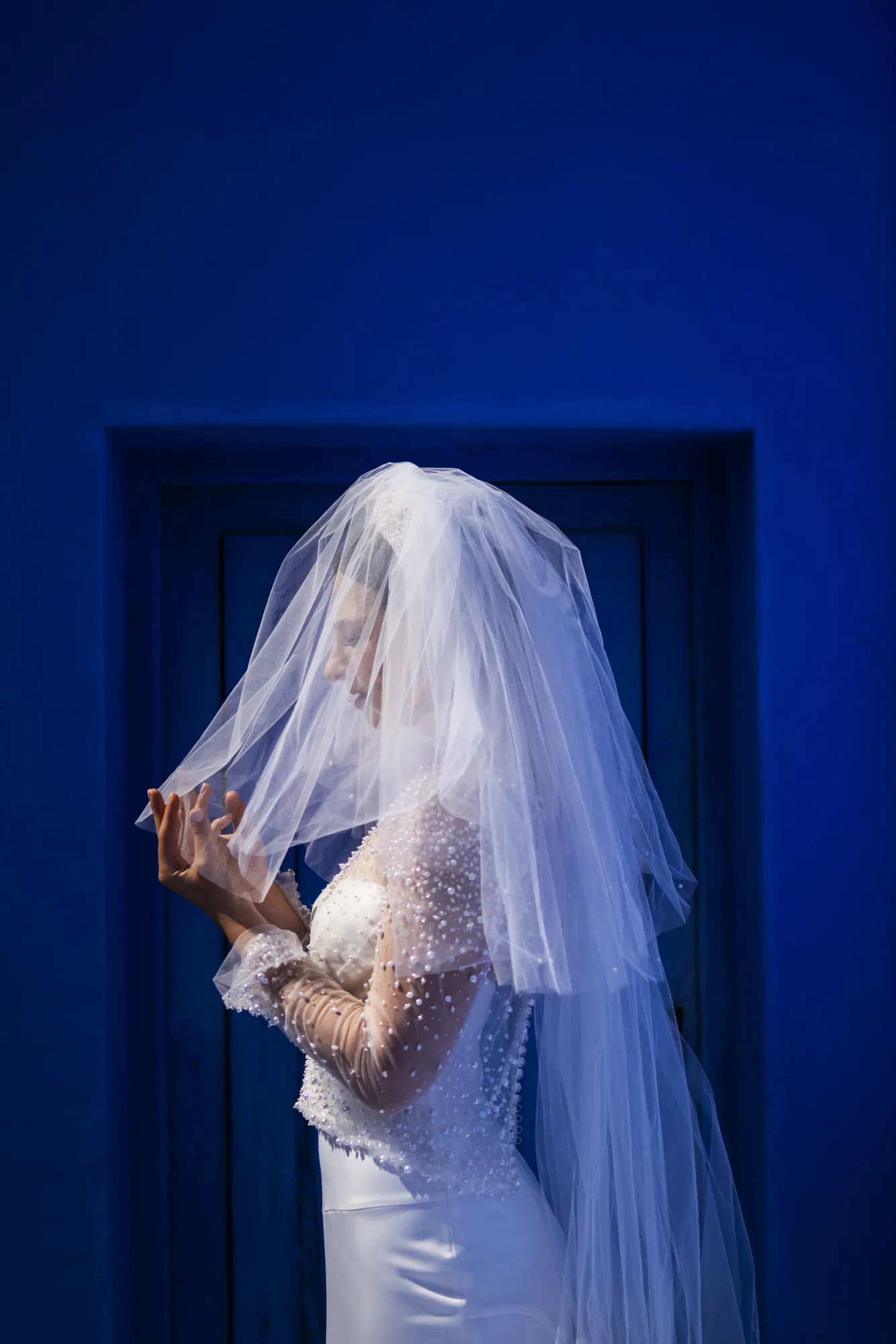 Bride lifting her veil before a deep blue door