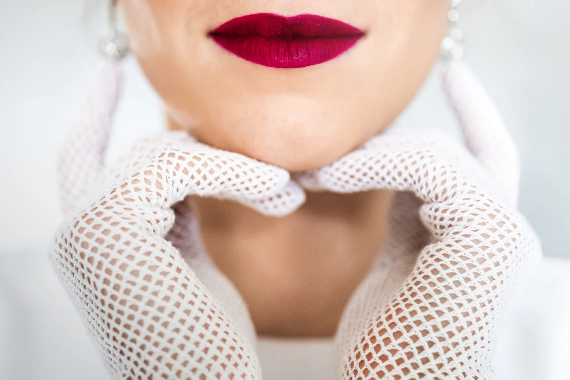 Bride's red lips framed by white lace gloves