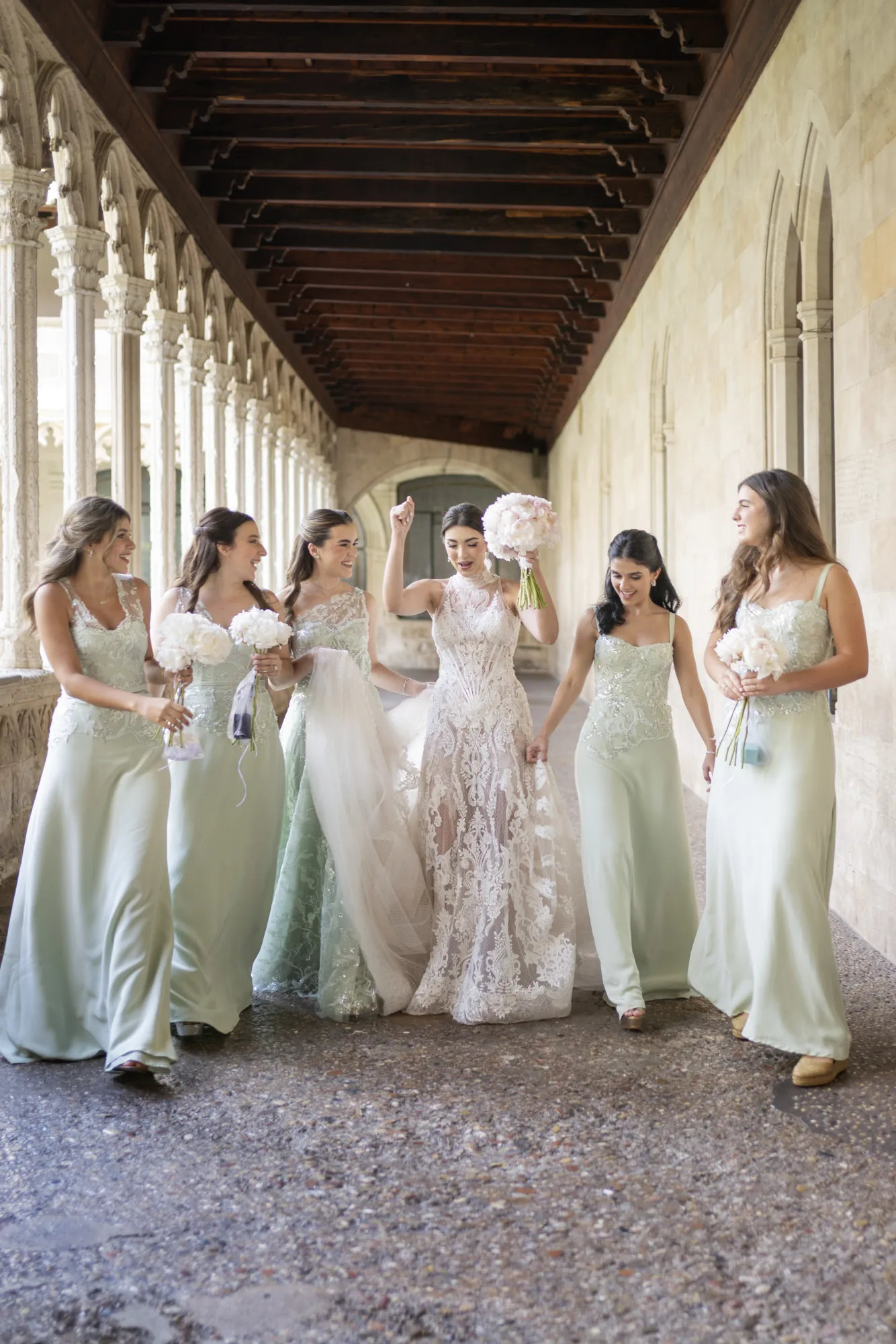 Bride walking with bridesmaids in sage green through a cloister