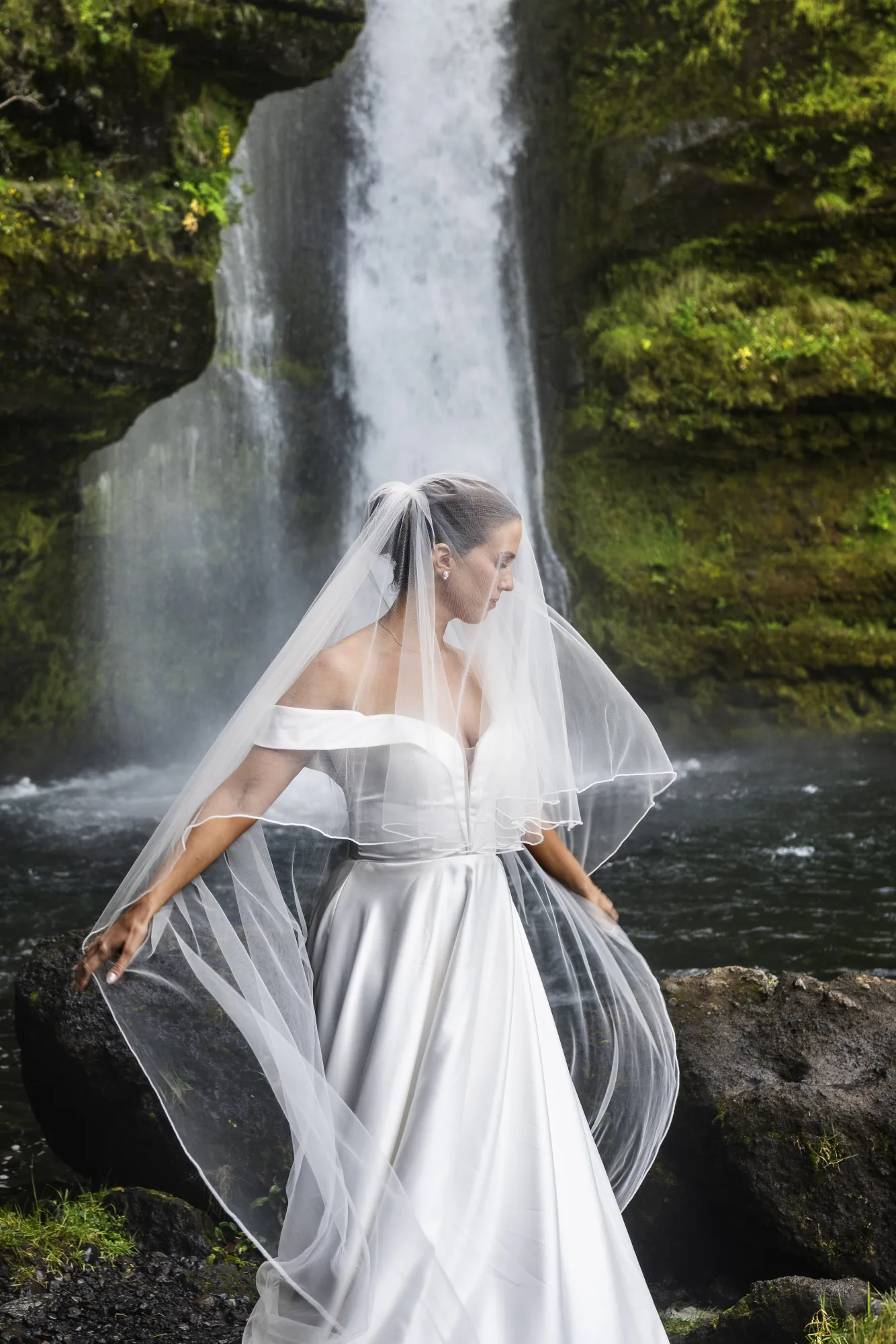 Bride with a long veil before a waterfall