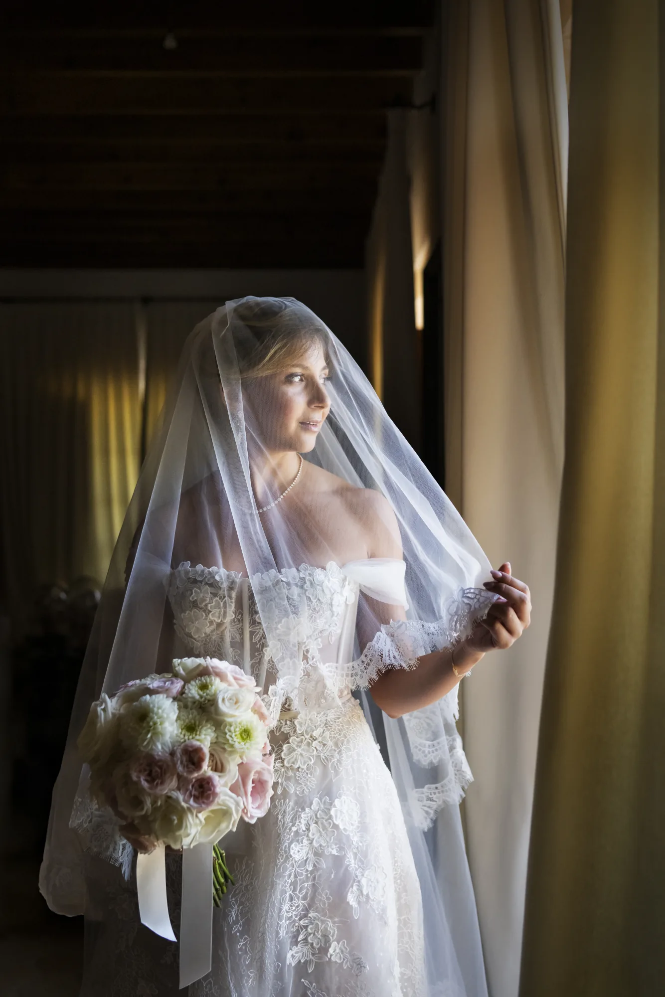 Bride with her veil and bouquet in soft window light