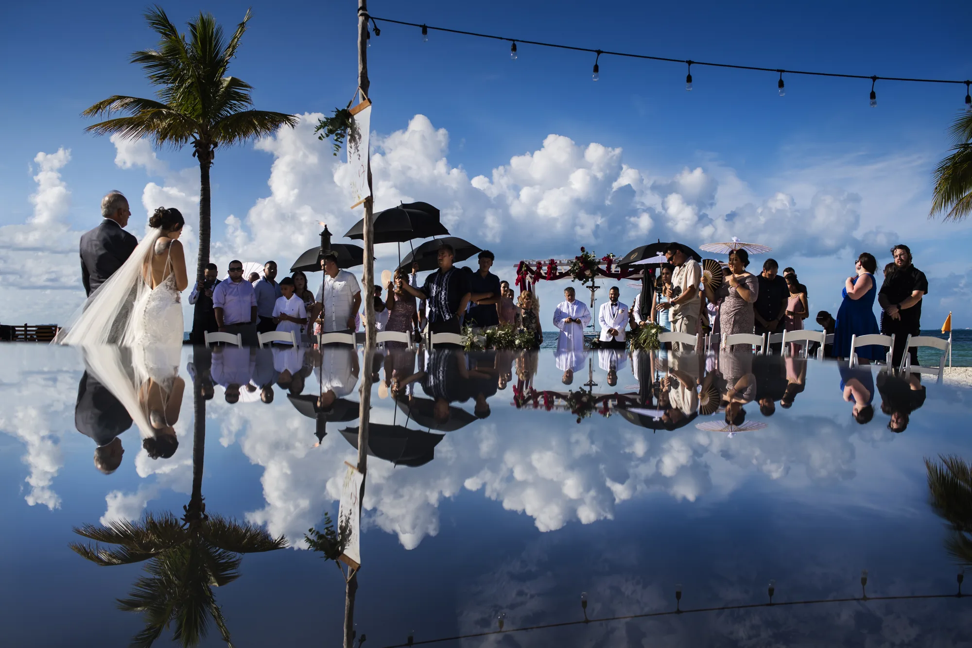Ceremony under palm trees mirrored in still water with clouds