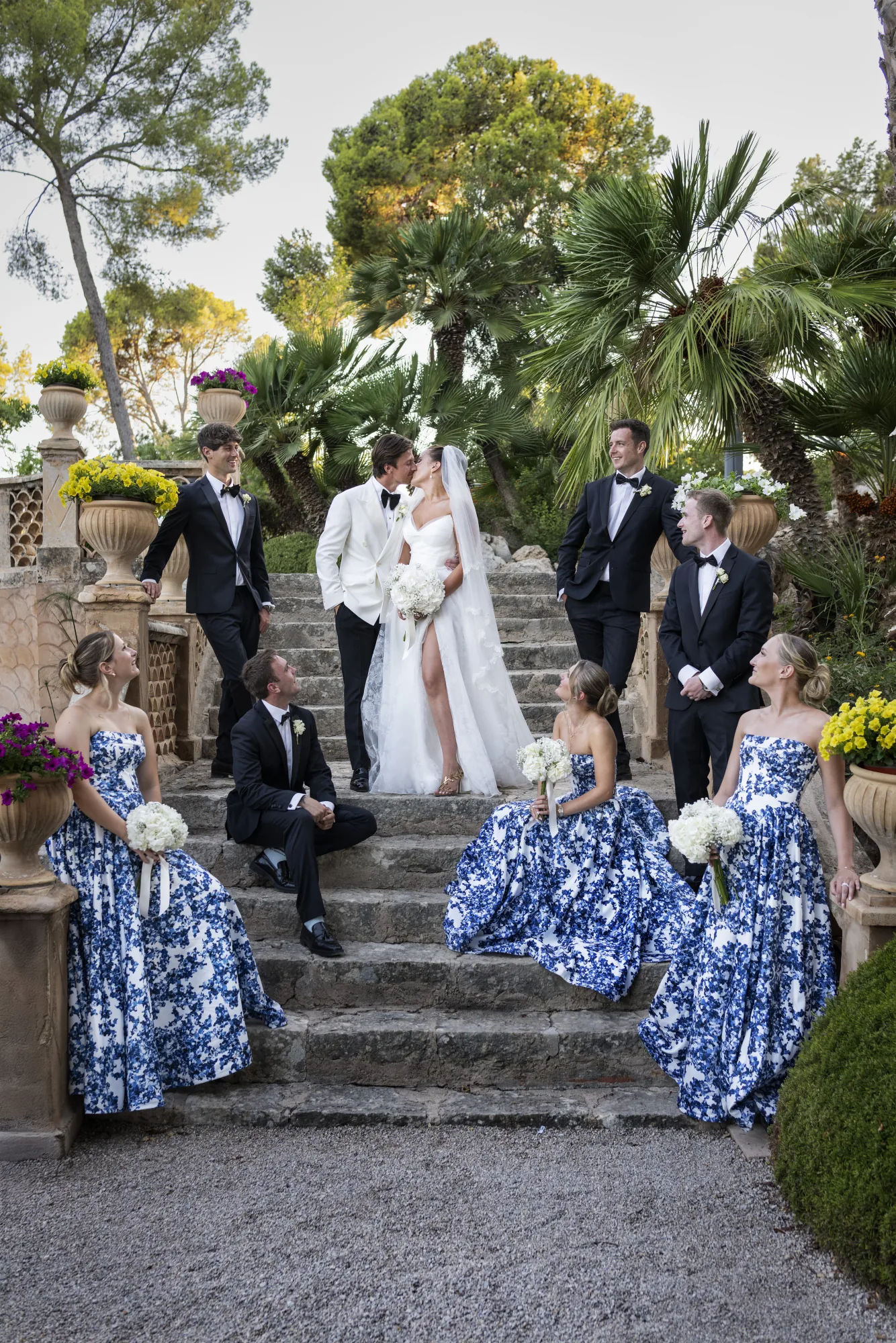 Couple and bridal party on garden steps, bridesmaids in blue print gowns