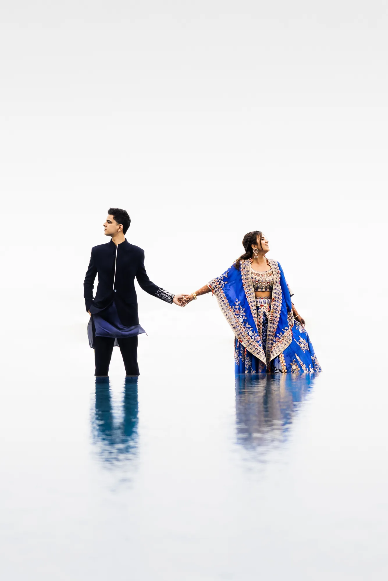 Couple hand in hand on a white reflective floor, the bride in blue