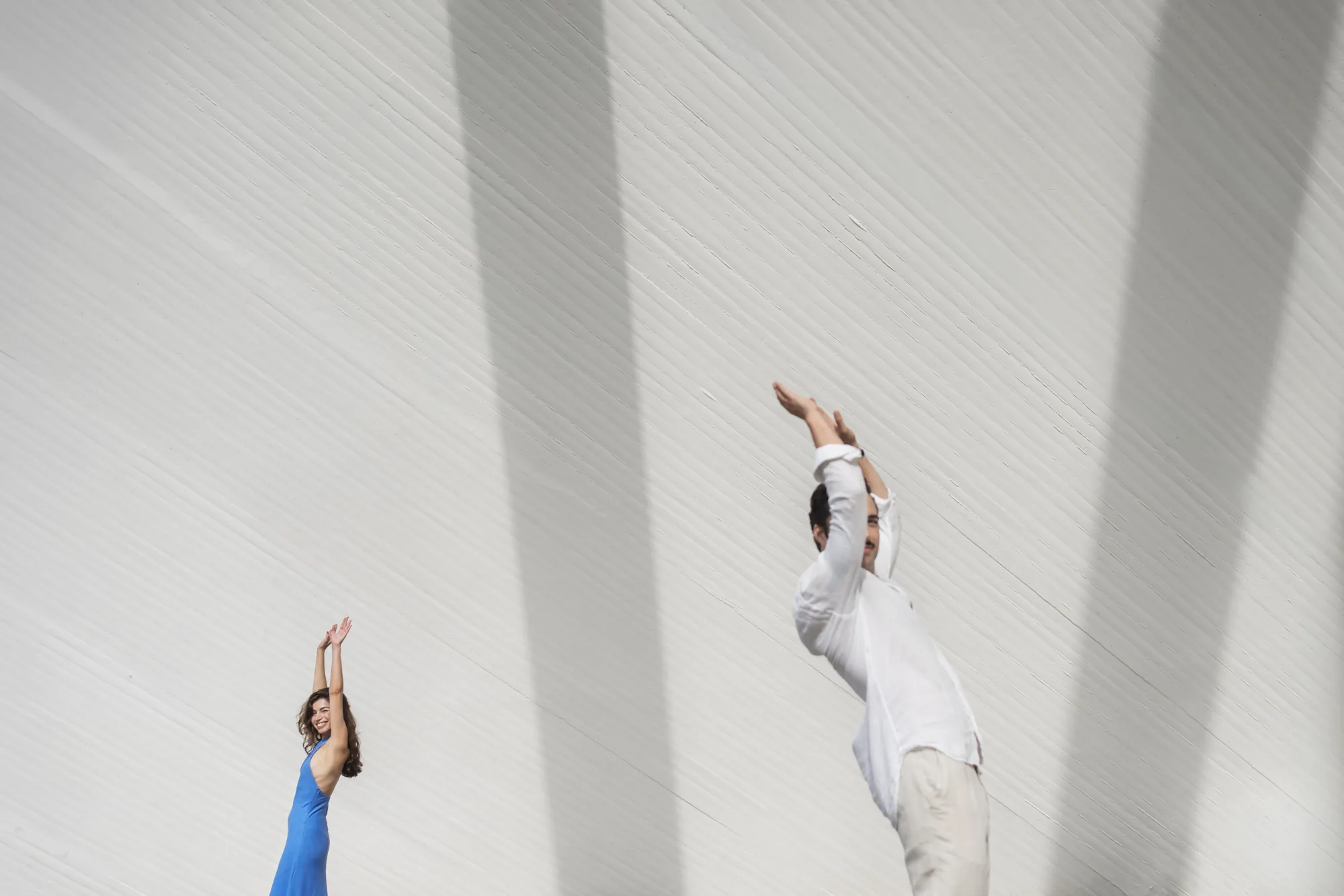Couple leaping beneath tall white concrete forms