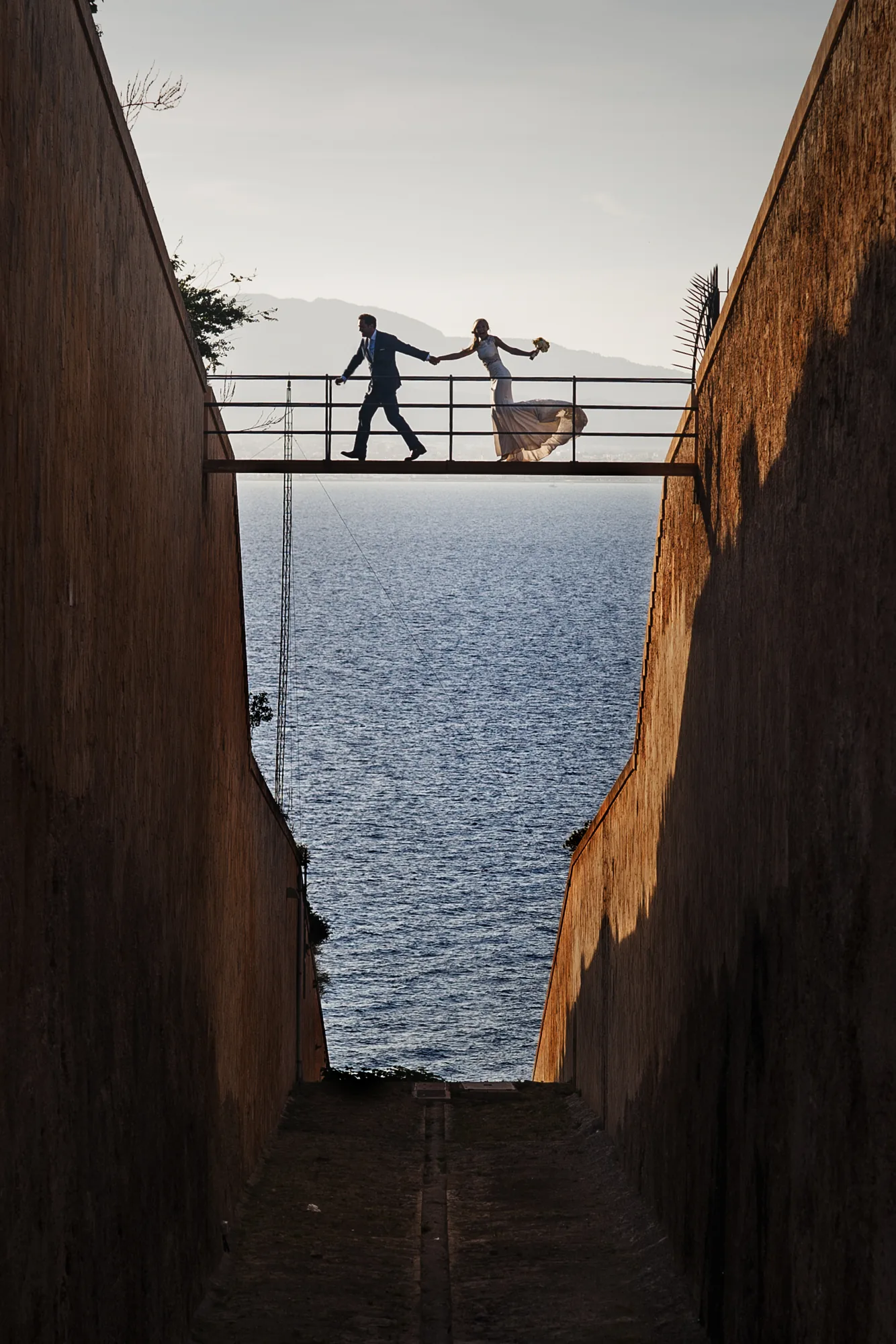 Couple on a narrow bridge between two walls above the sea