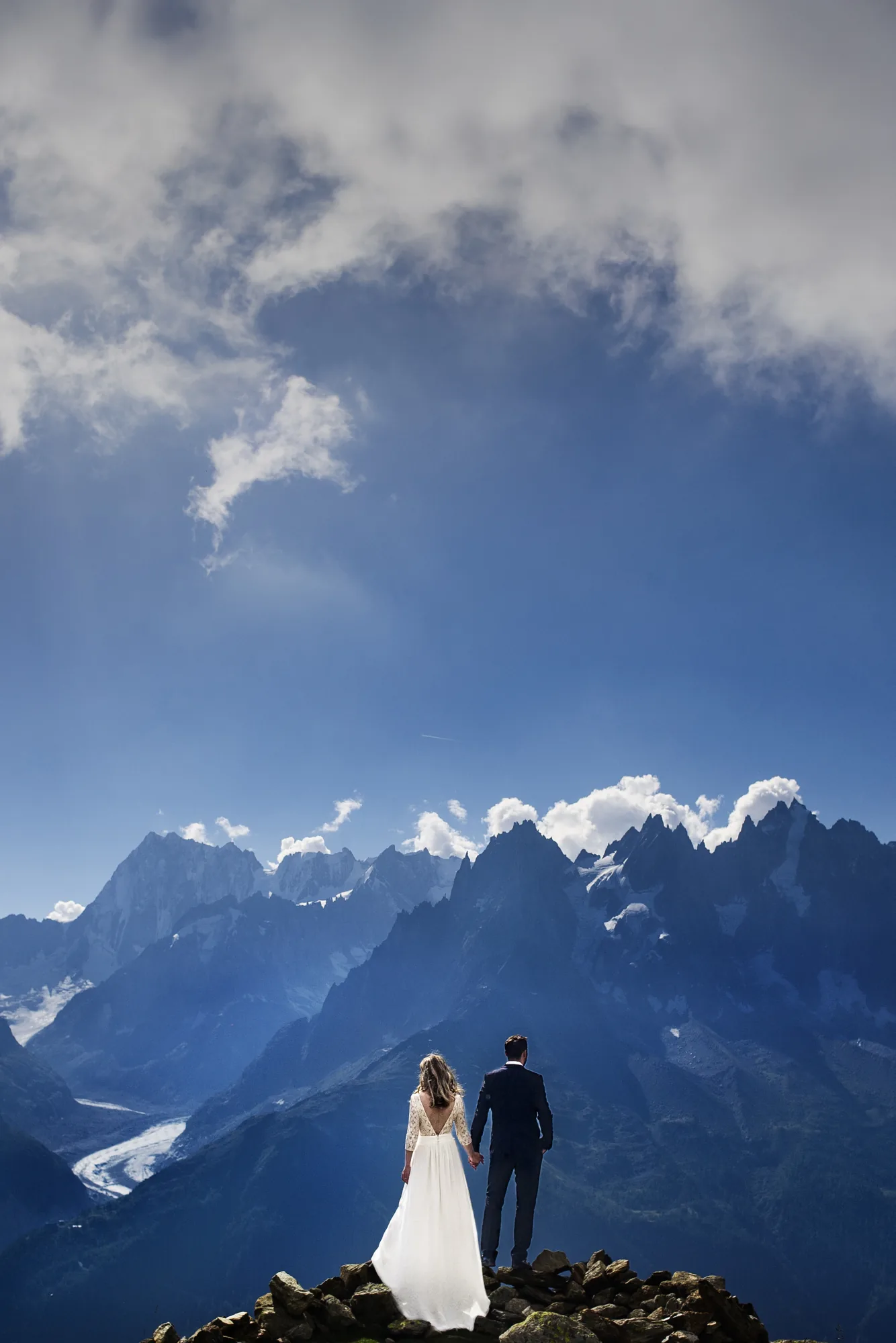 Couple standing before snow-capped peaks under a blue sky