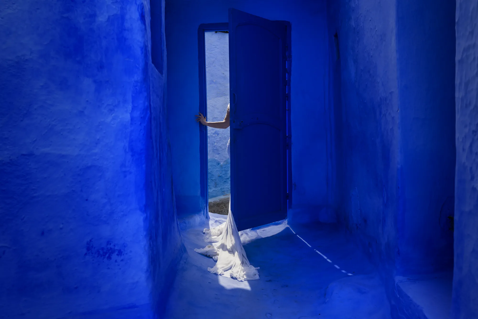 Deep blue corridor opening onto a sunlit doorway