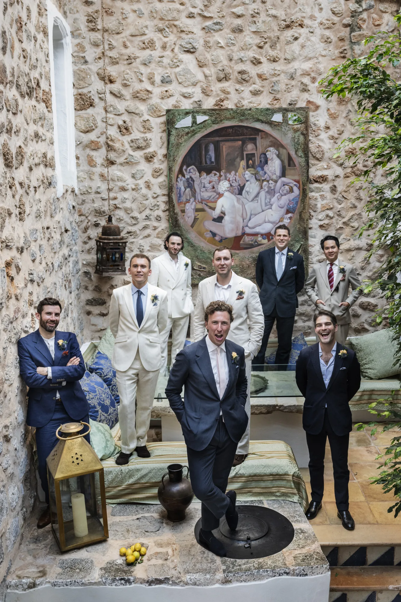 Groom and groomsmen in a stone courtyard beneath a painted mural