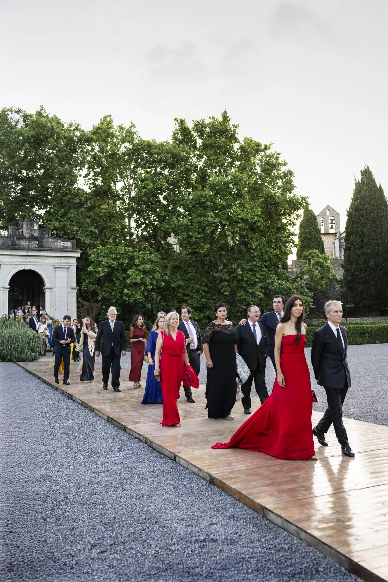 Guests walking in procession along a garden path, a woman in red at the front