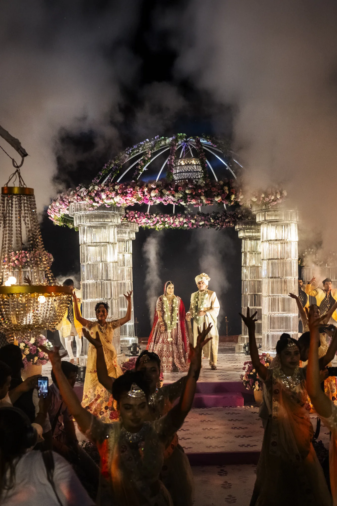 Indian wedding mandap at night, guests celebrating through coloured smoke