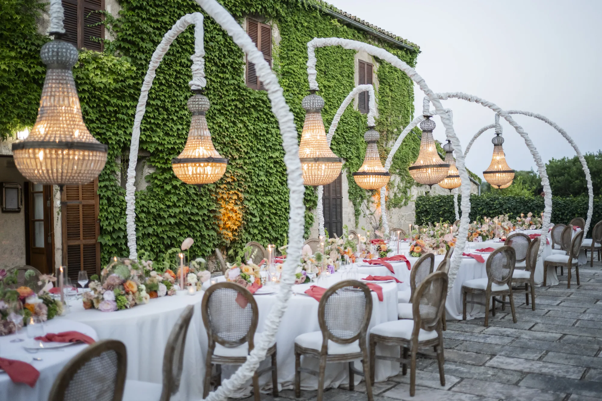 Long reception table under chandelier arches against an ivy wall