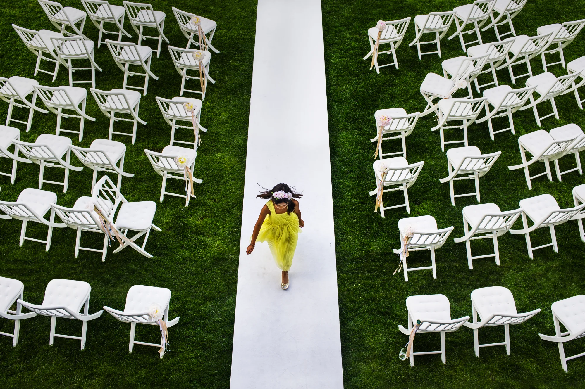 Overhead view of a guest walking a white aisle between chairs on a lawn