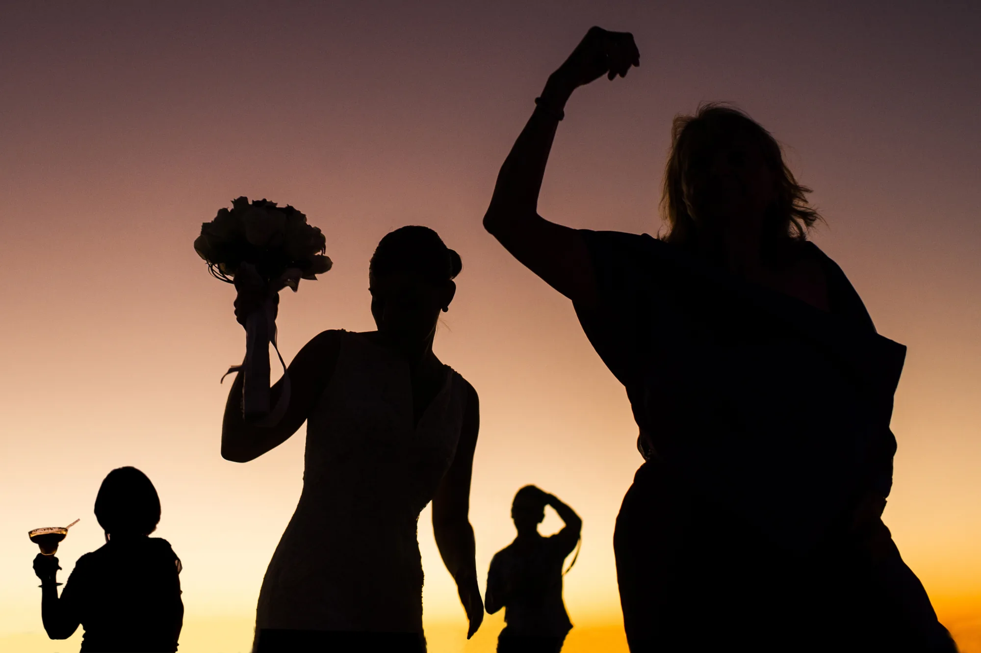 Silhouettes of guests raising a bouquet against an orange sky