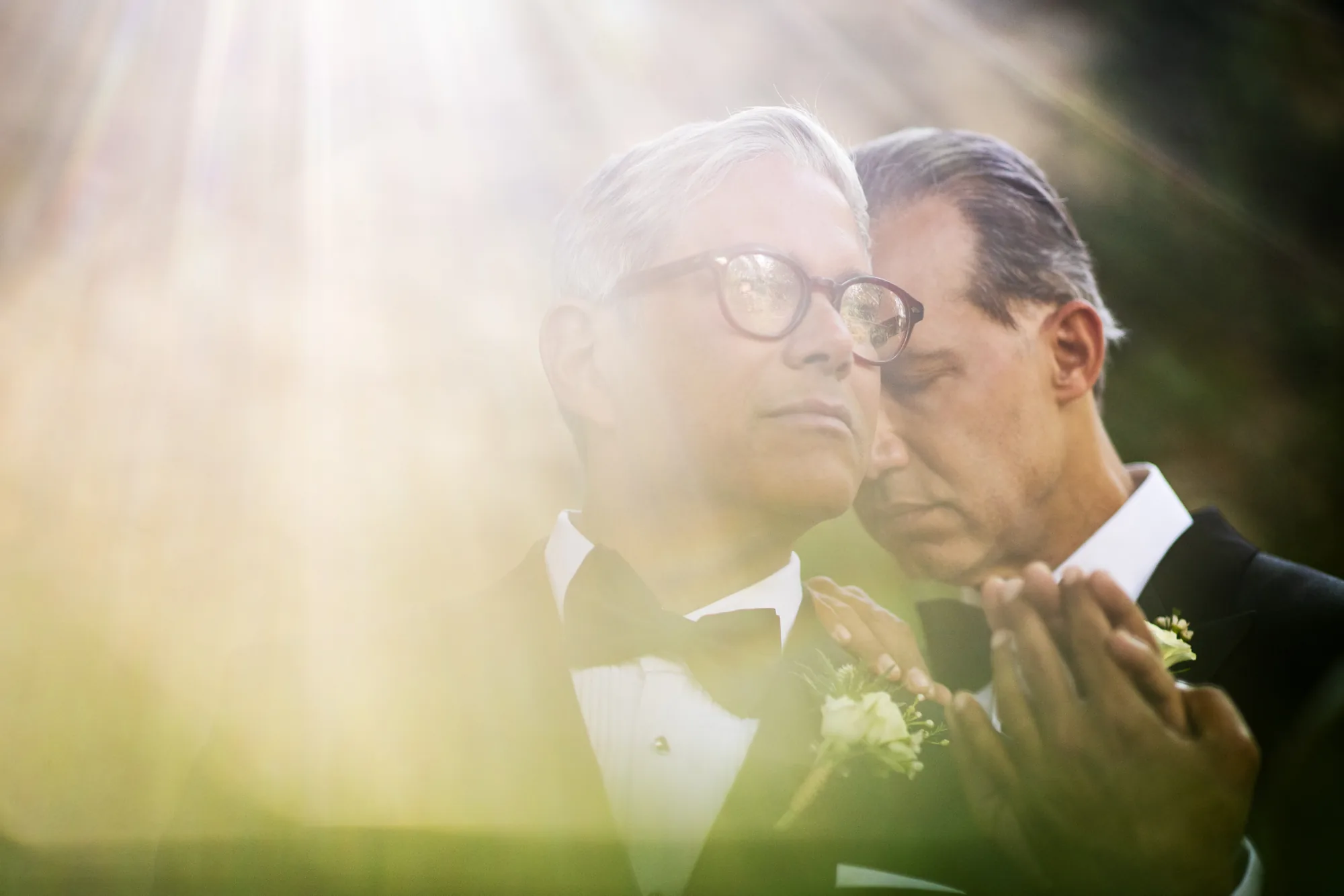 Two men embracing cheek to cheek in a sun flare