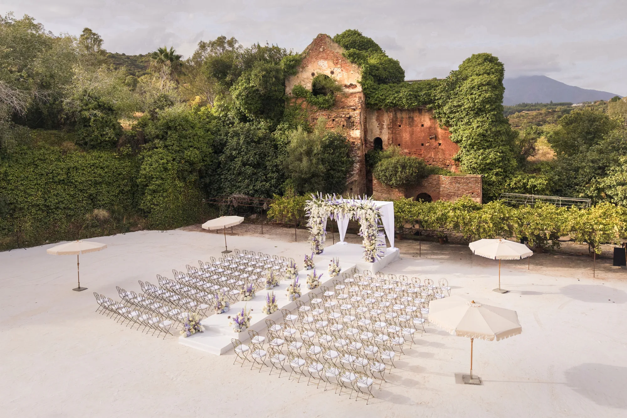 White ceremony set up on a terrace beside ivy-covered ruins